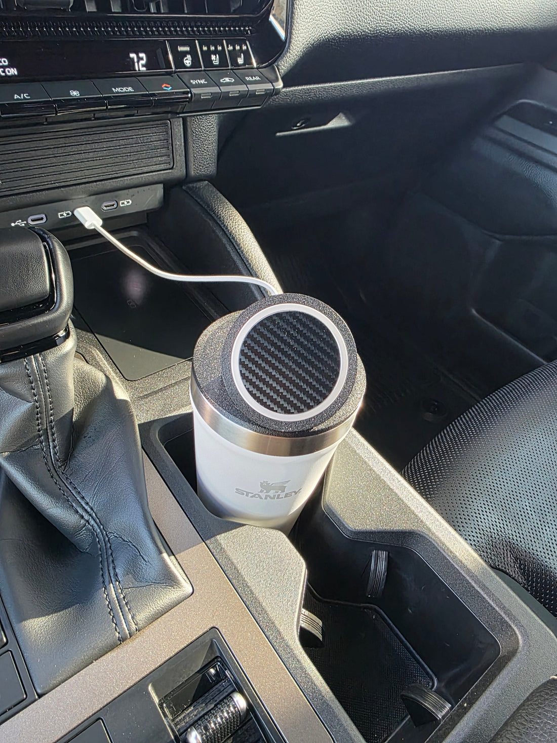 White Stanley 16 oz cup with the NMT MagSafe mount as its lid, sitting in a truck cupholder with the charging cable running to the dash