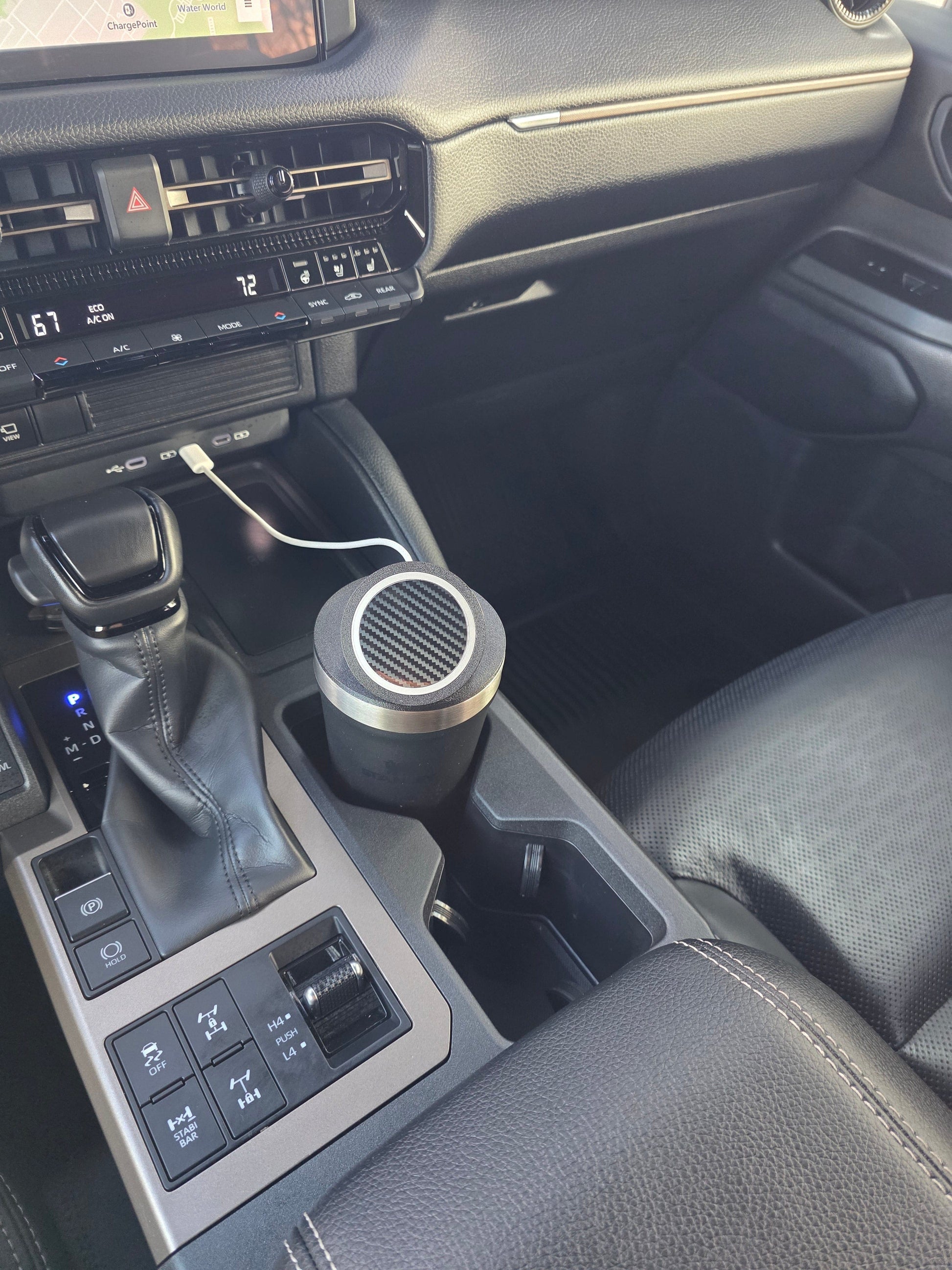 Dark tumbler with the MagSafe stand lid in a truck console cupholder, charging cable plugged into the dash