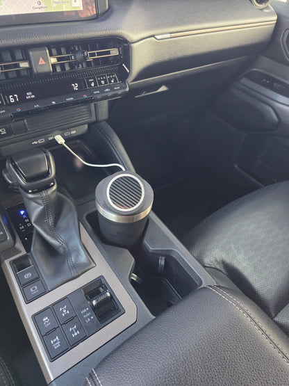 Dark tumbler with the MagSafe stand lid in a truck console cupholder, charging cable plugged into the dash