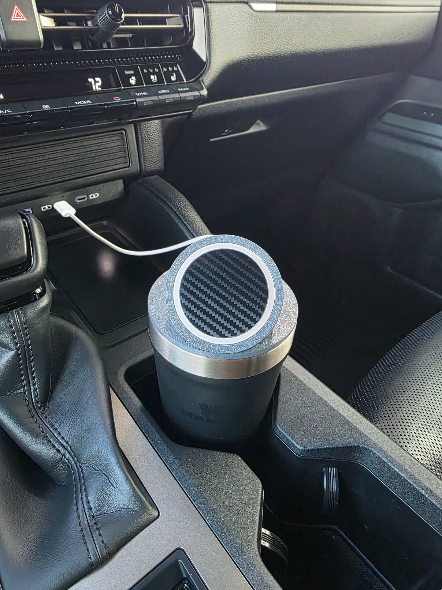 Dark tumbler wearing the MagSafe stand lid in a truck cupholder, cable routed from the dash port