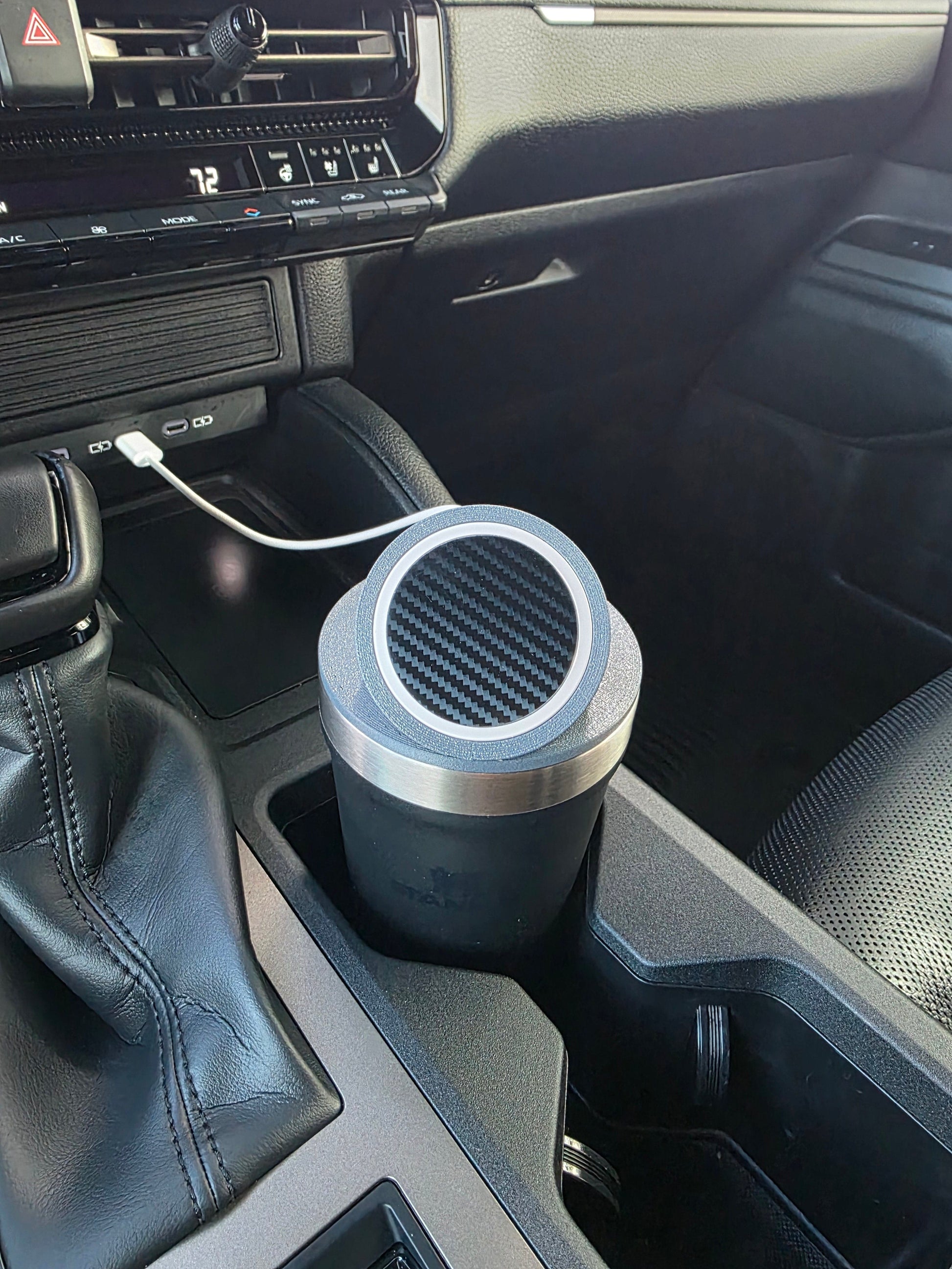 Dark tumbler wearing the MagSafe stand lid in a truck cupholder, cable routed from the dash port