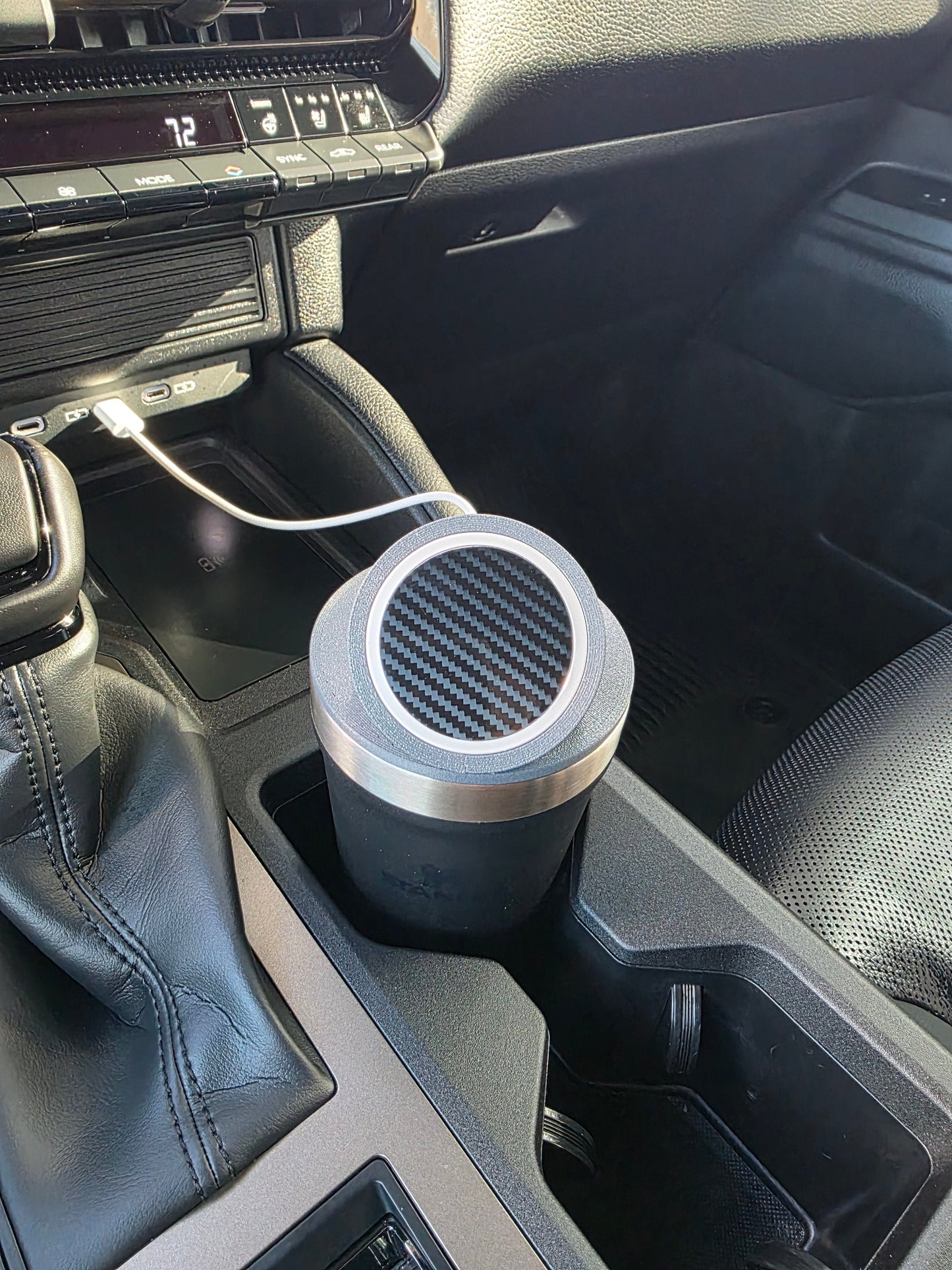 MagSafe stand lid on a dark tumbler in a truck console cupholder, charging cable connected