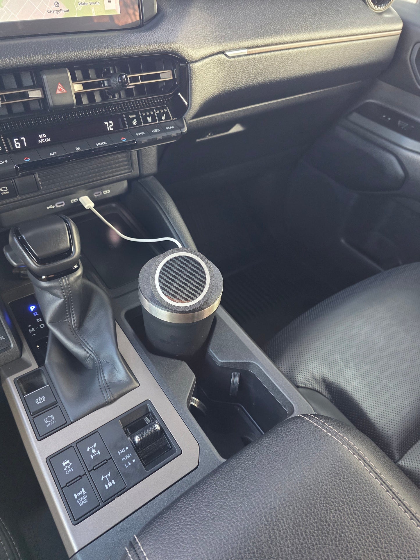 Dark tumbler with the MagSafe stand lid in a truck console cupholder, cable running from the dash