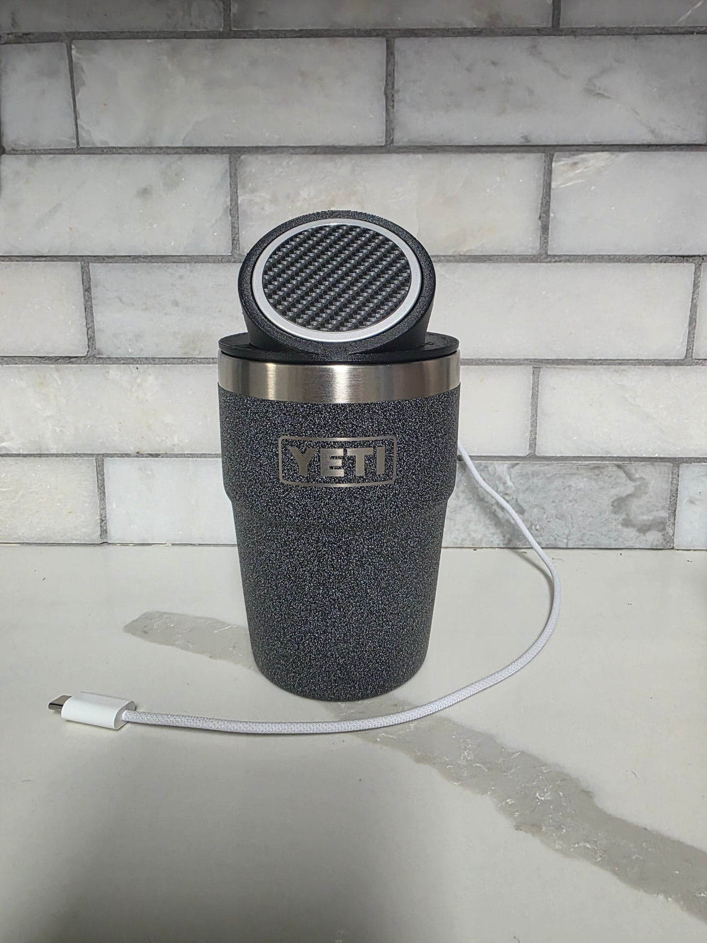 YETI cup wearing the black MagSafe stand lid on a kitchen counter with a USB-C charging cable