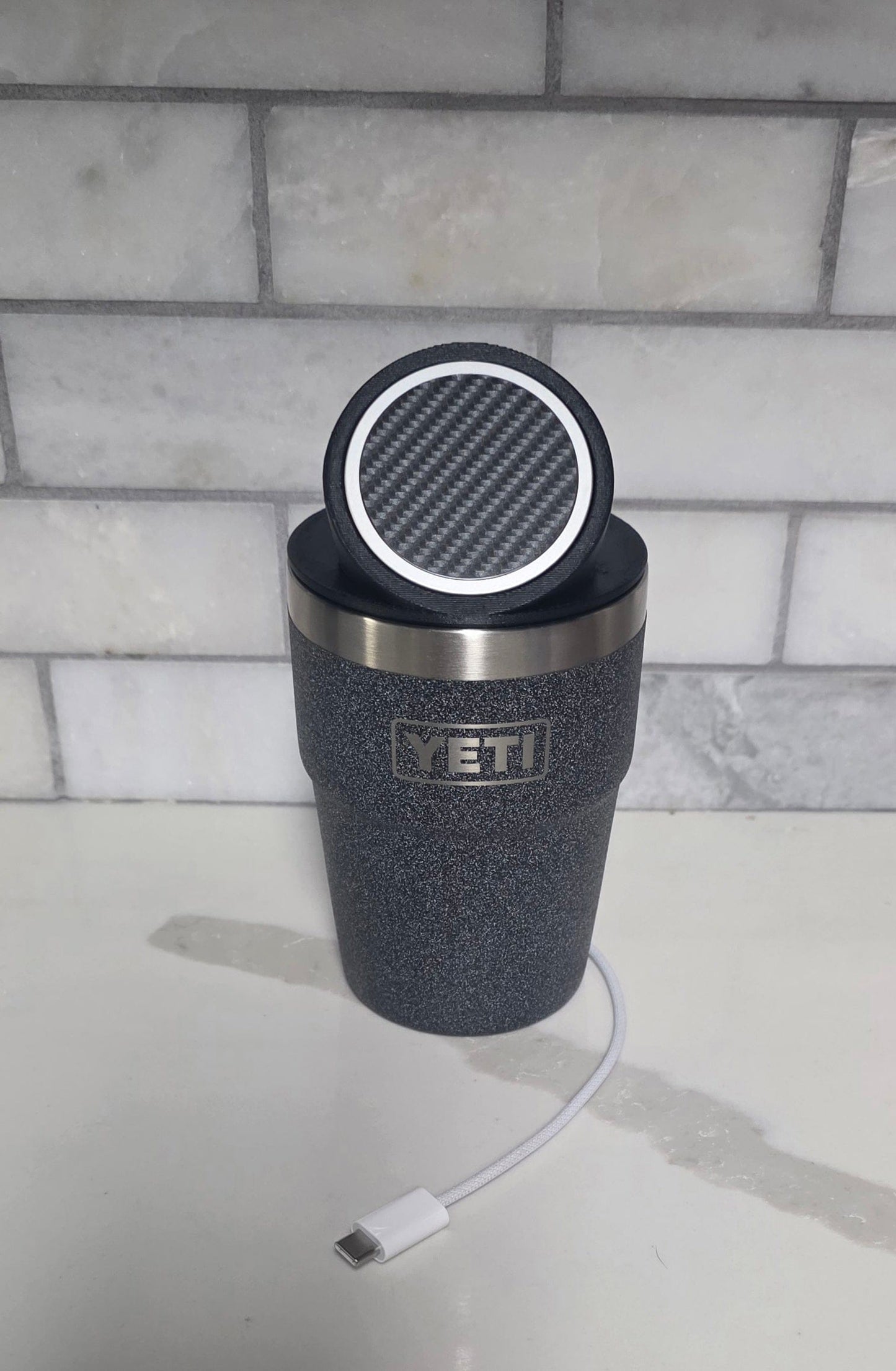 YETI cup with the black MagSafe stand lid tilted up on a kitchen counter, USB-C cable alongside