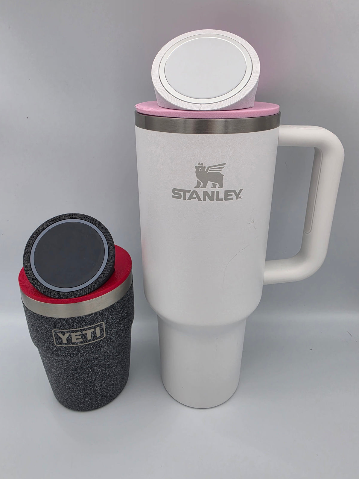 A tall Stanley with a pink mount and white top ring beside a shorter YETI with a red mount and black top ring
