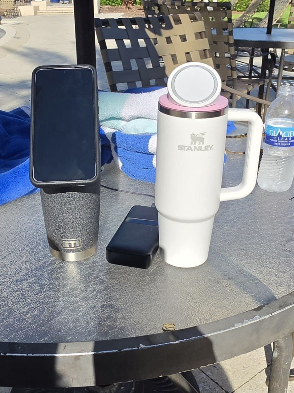 Phone on the MagSafe stand on a YETI cup on a patio table, Stanley cup beside it